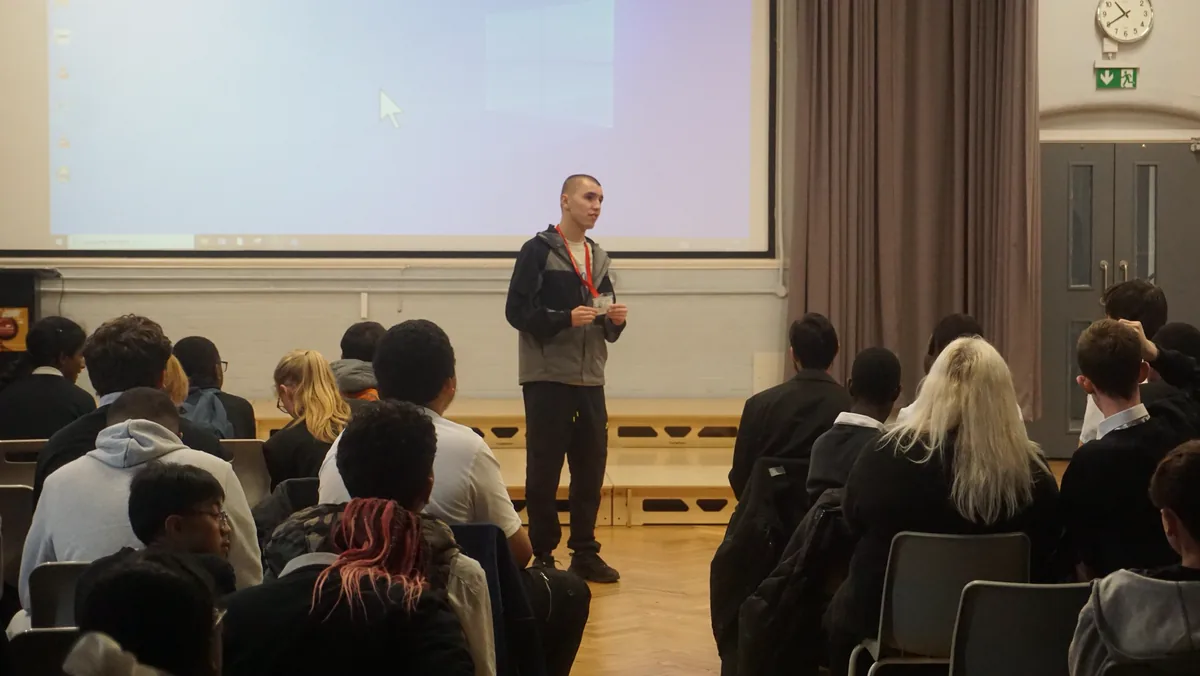 Ensie standing at the front of the hall speaking to a seated audience of students.