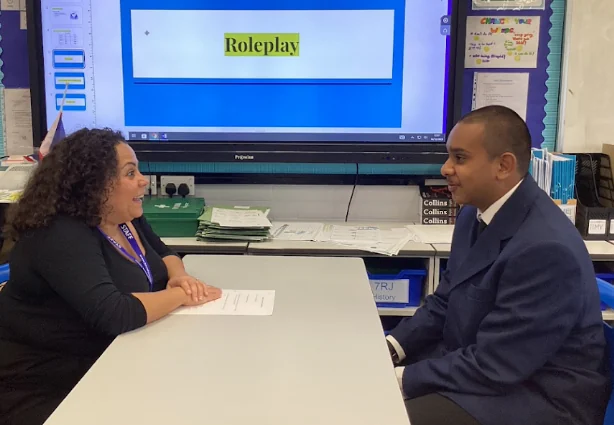 A student sitting opposite a member of staff for a practice interview, a whiteboard behind them reading “Roleplay”.