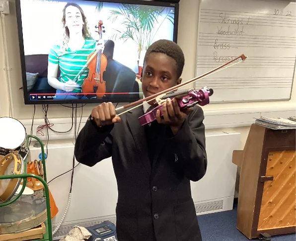 A student playing a violin in front of a screen showing a violin teacher.