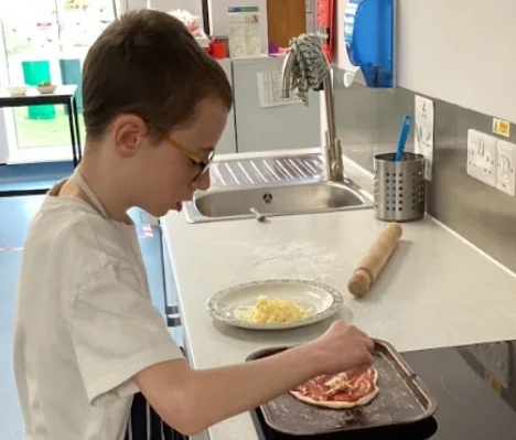 A student preparing food at a kitchen worktop, grated cheese and a rolling pin beside the tray.