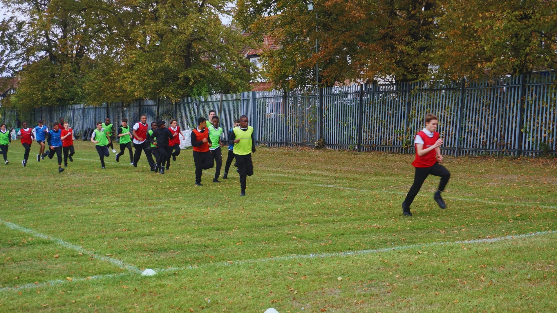 Students in coloured bibs running across the school field during a games lesson.