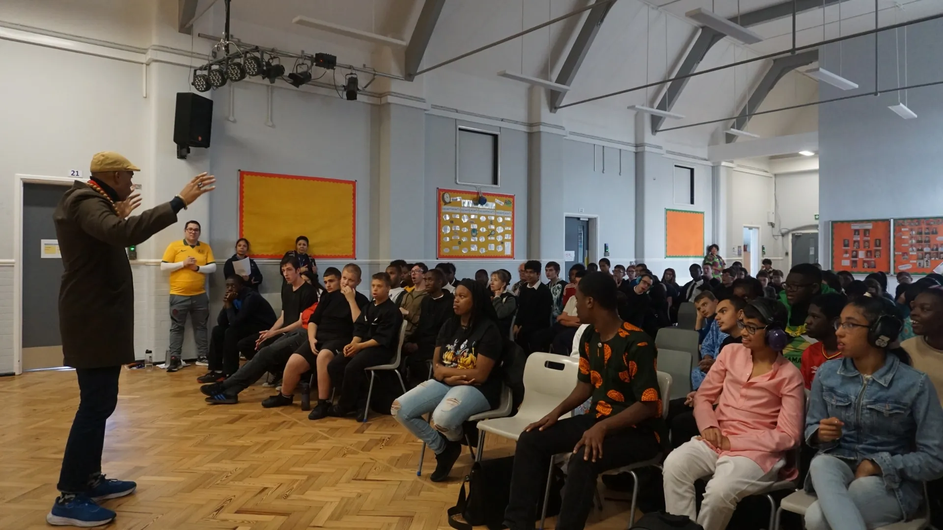A visiting speaker addressing a hall full of seated students during an assembly.
