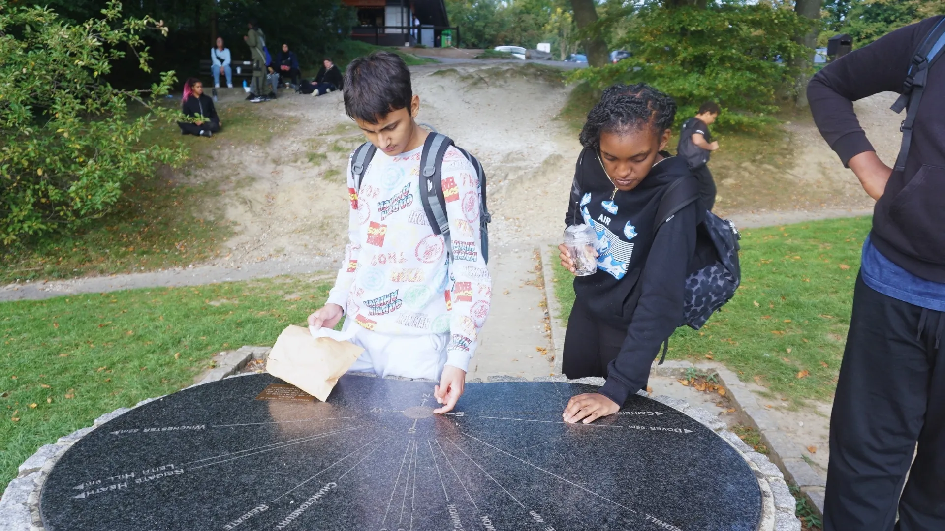 Students walking across a paved outdoor space, one carrying a folded map.