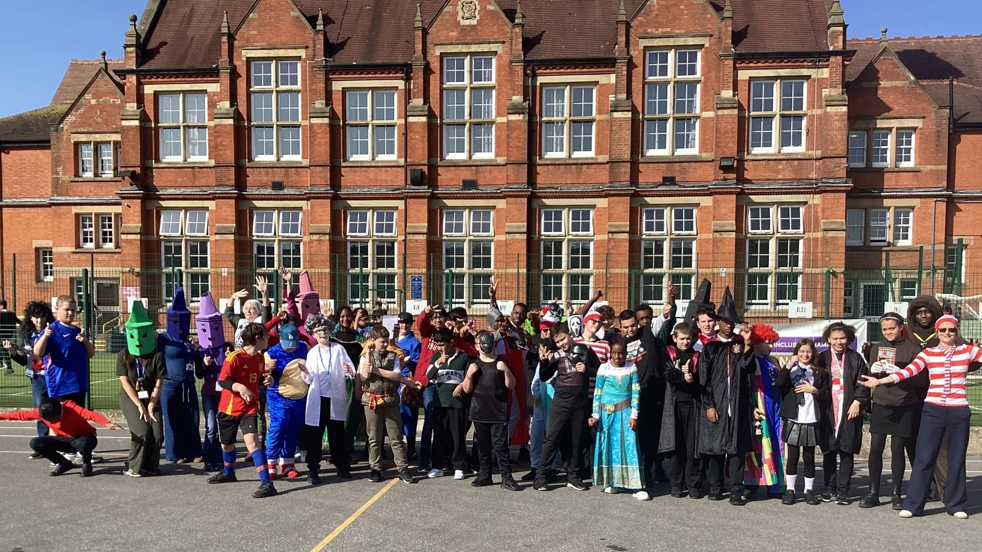 Students in World Book Day costumes lined up across the playground in front of the school building.