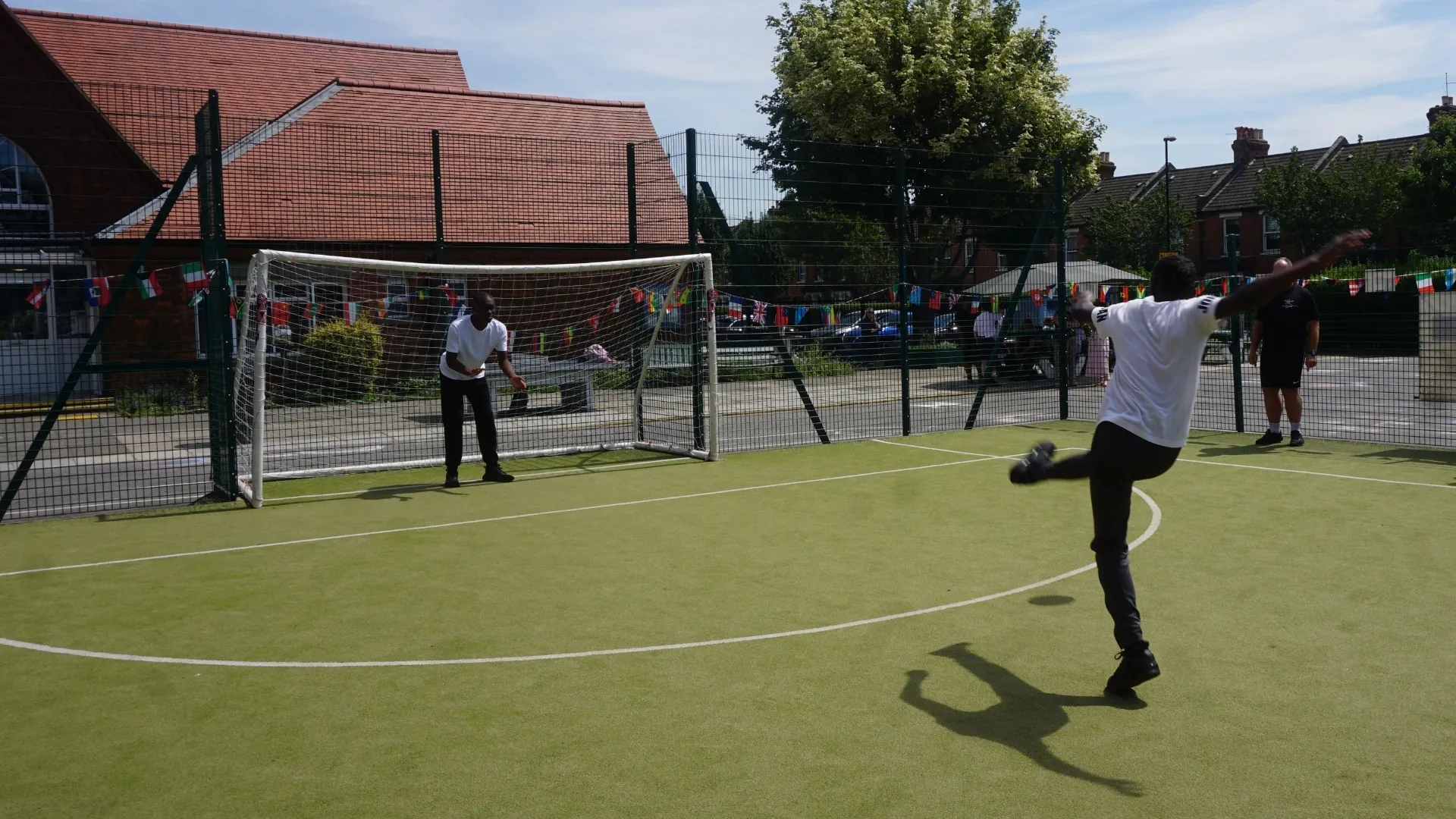 A student taking a shot at goal on the all-weather pitch, a member of staff keeping goal.