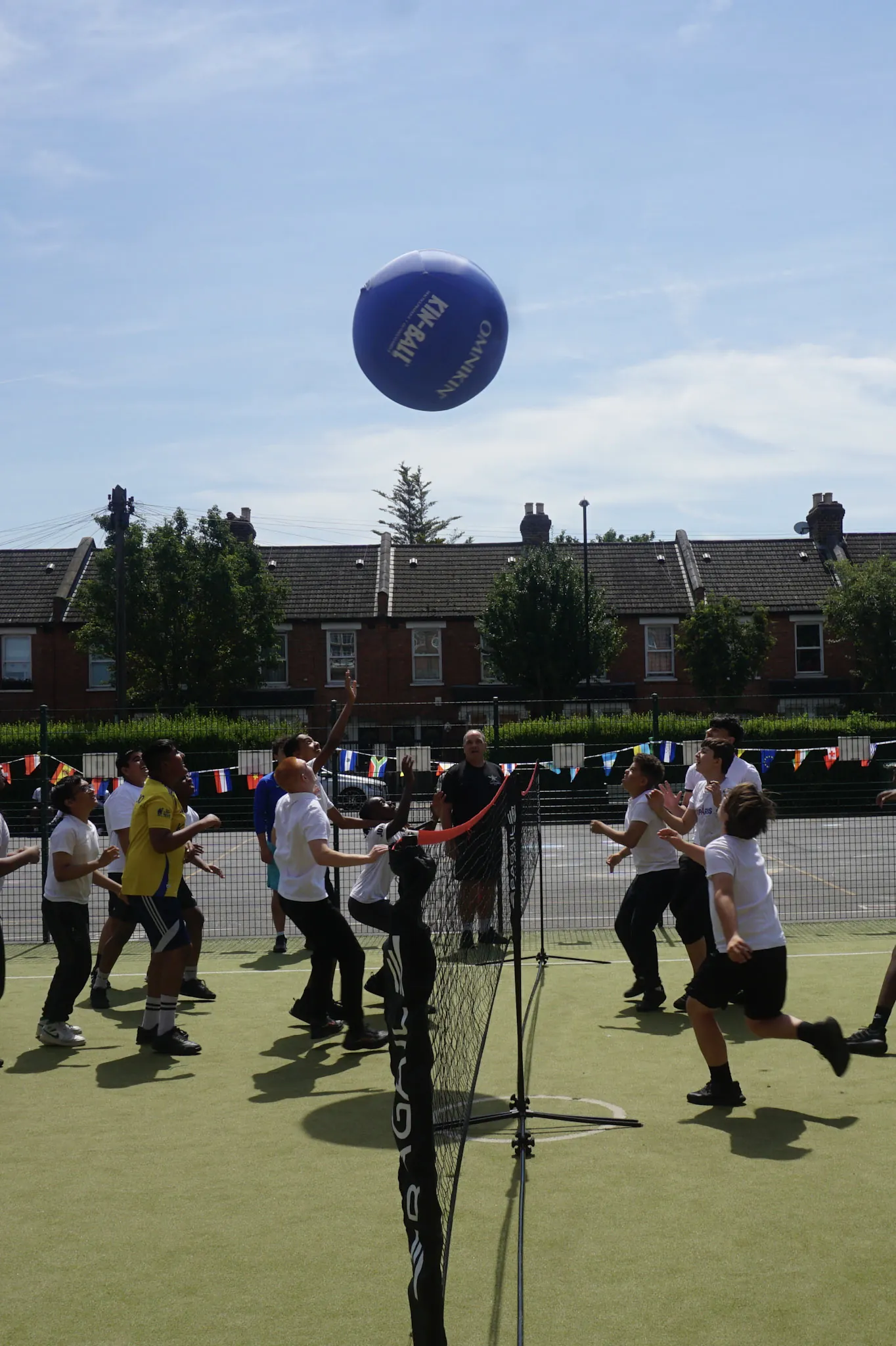 Students on the all-weather pitch reaching for a large blue kin-ball high in the air, bunting strung across the fence behind them.
