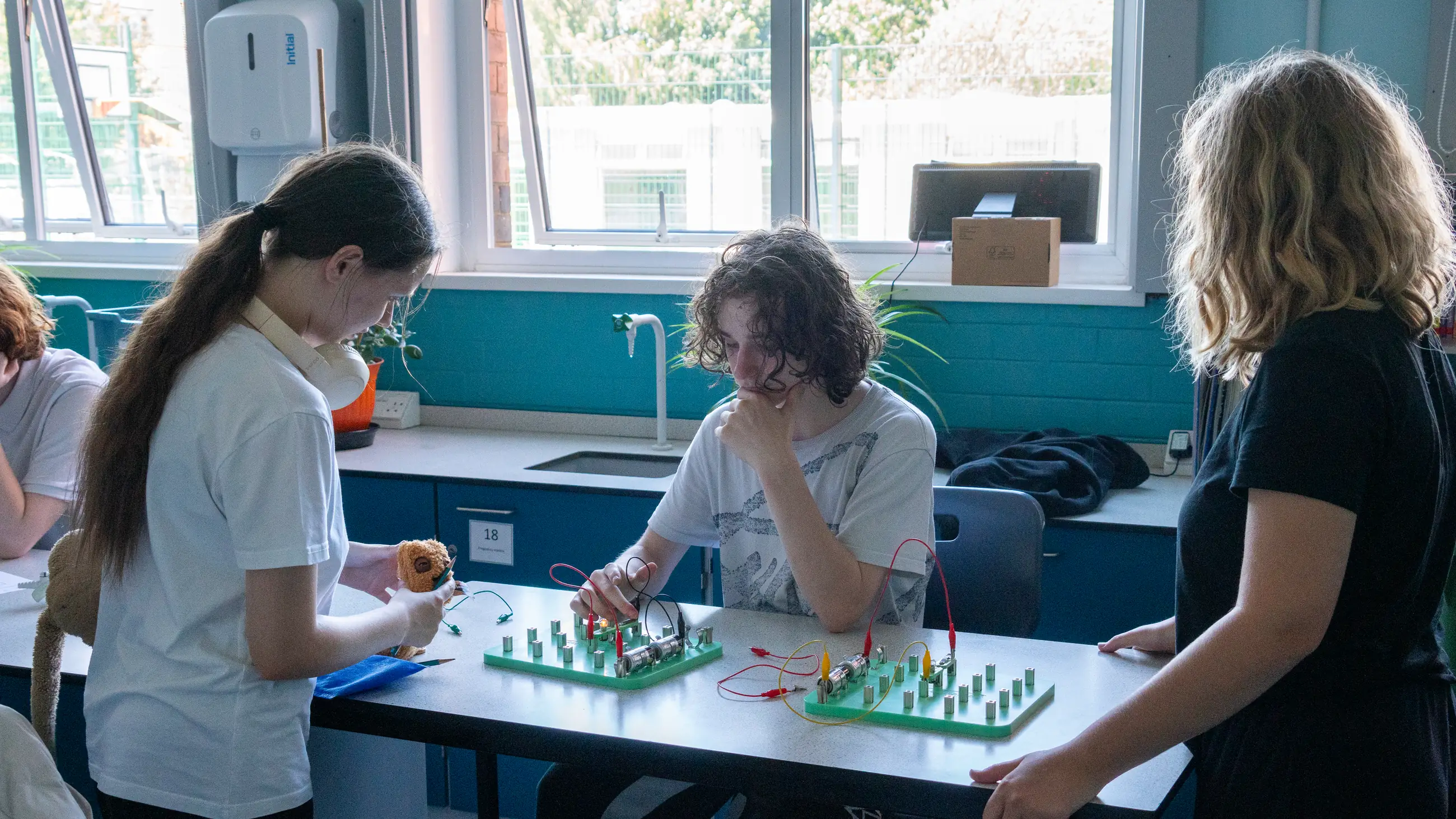 Students working at a laboratory bench with a member of staff, model boards laid out in front of them.