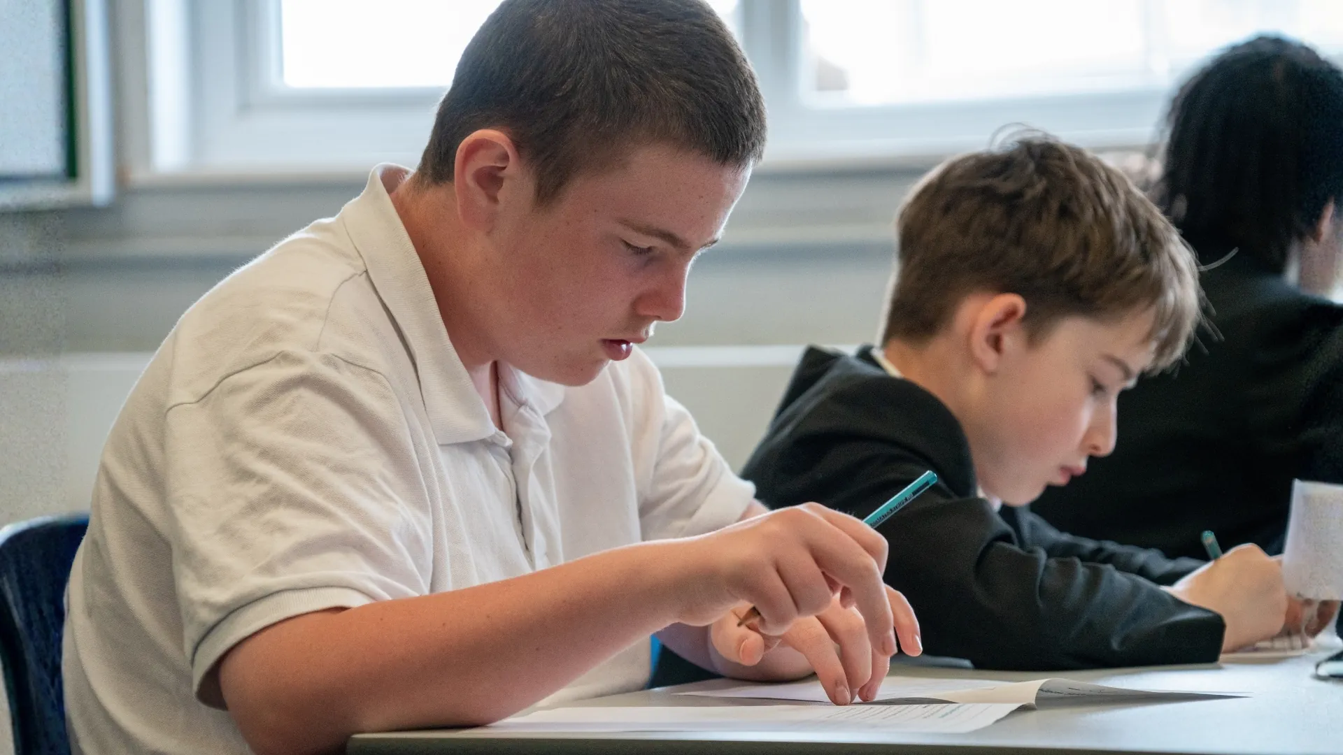 Two students writing at a desk, working through the same task.
