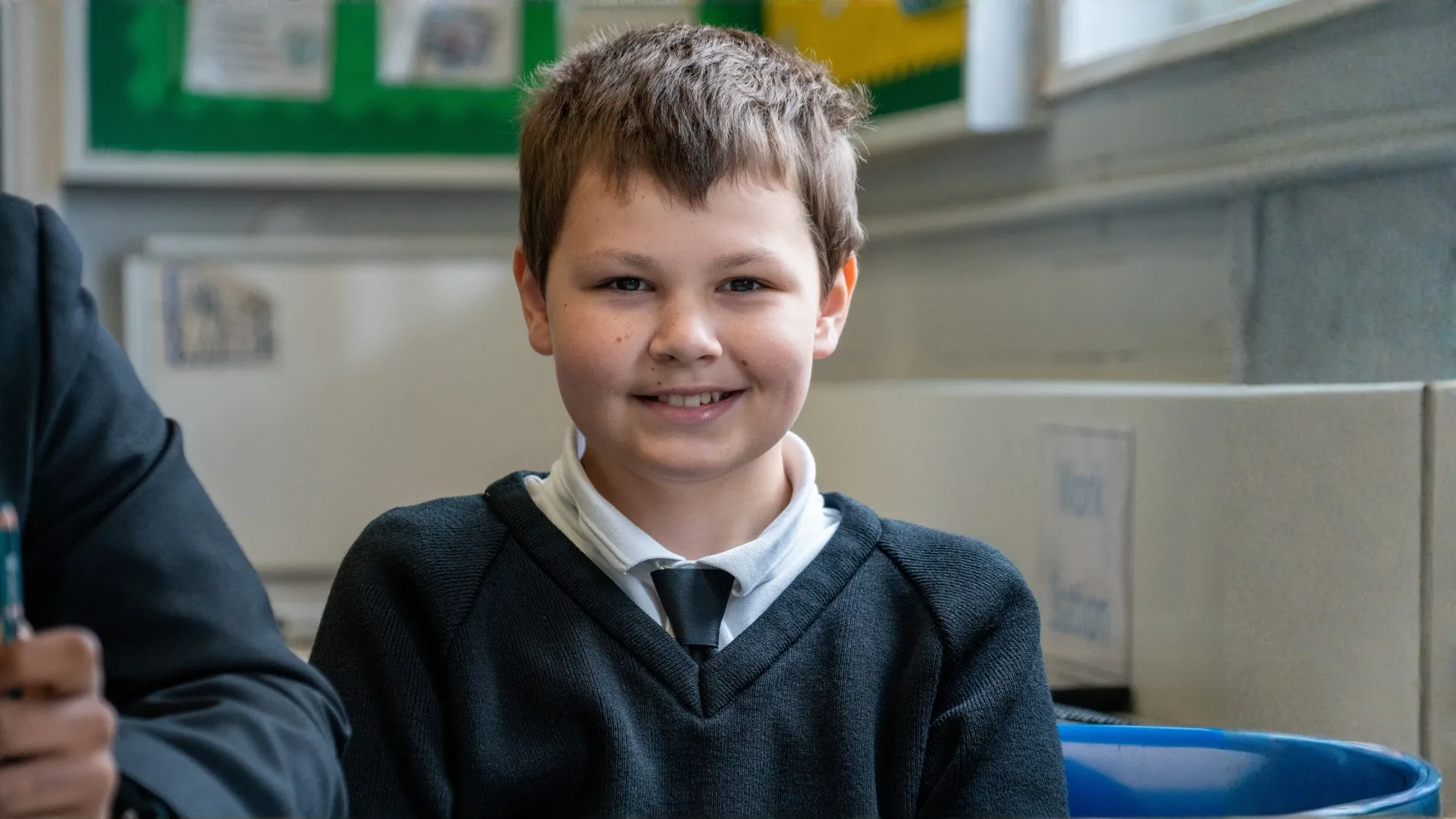 A student in school uniform smiling at the camera during a lesson.