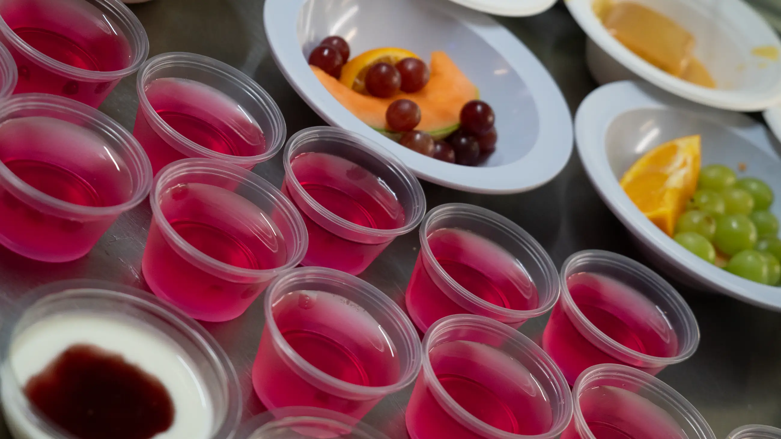 Pots of set jelly and plates of chopped fruit laid out on a kitchen counter.