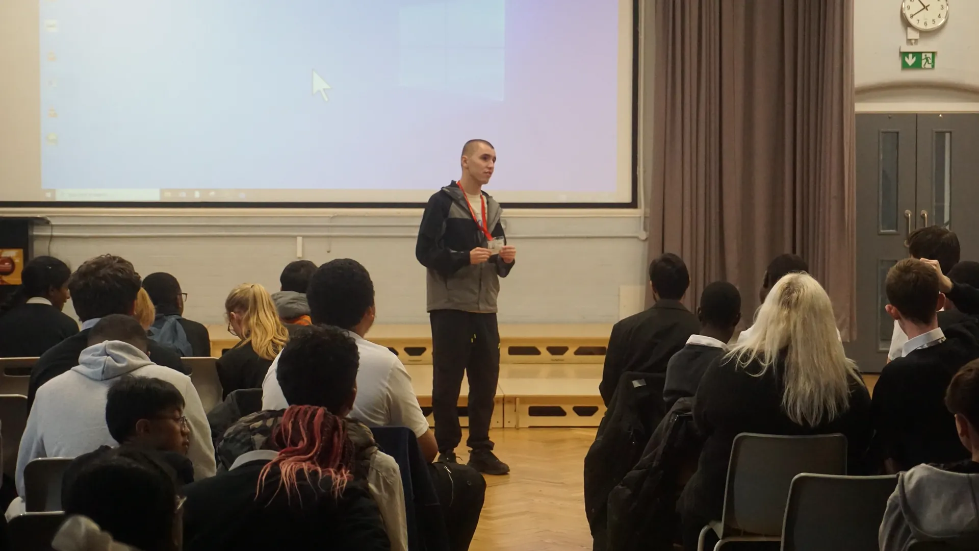 A former student speaking to a hall of seated students and staff.