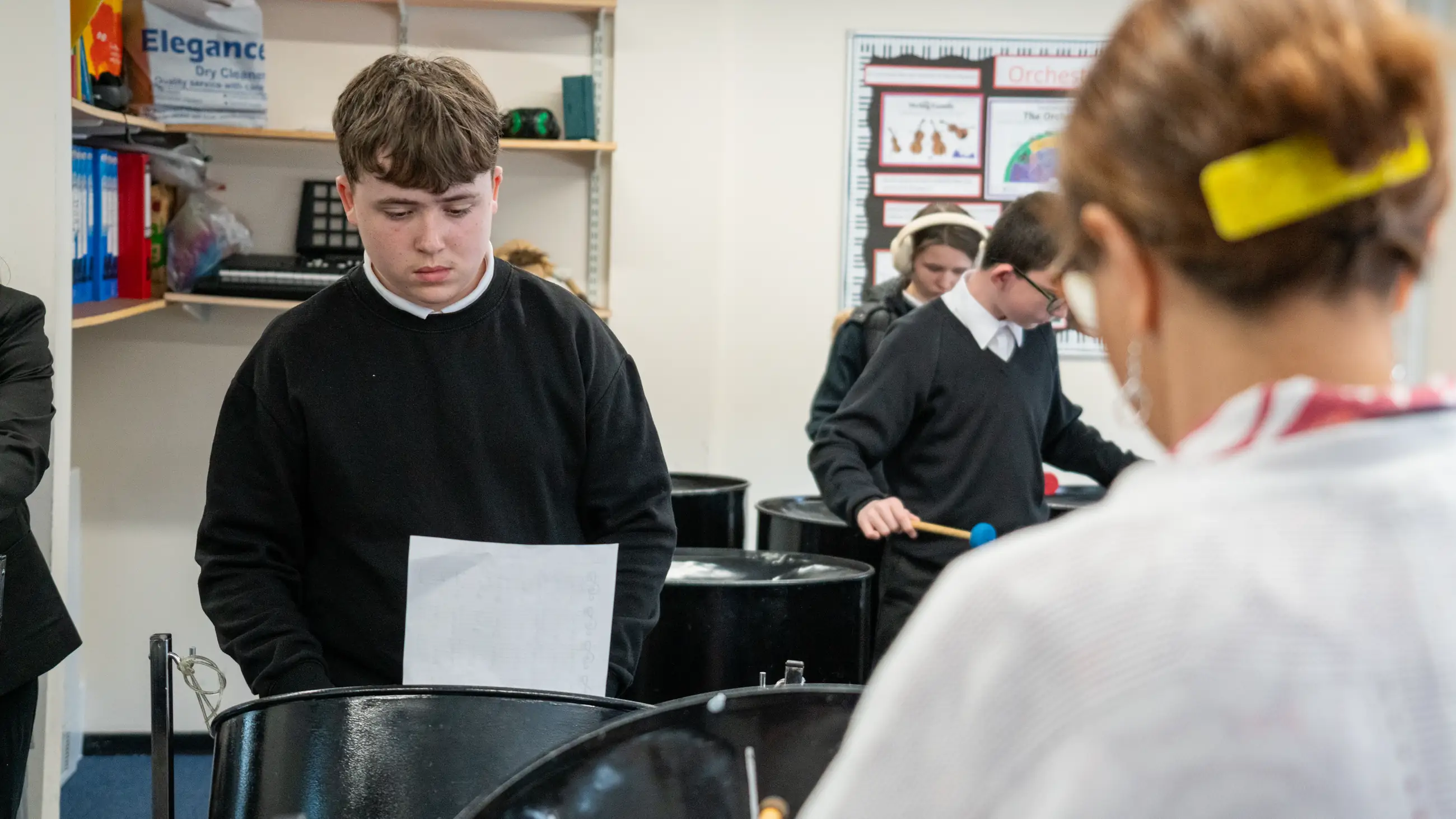 A student playing a steel pan, classmates at other instruments behind.
