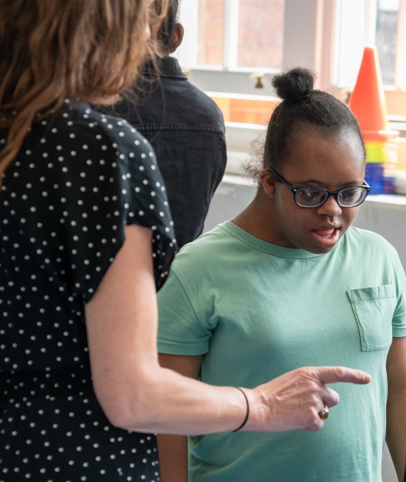 A member of staff talking with a student in a classroom, gesturing as they speak.