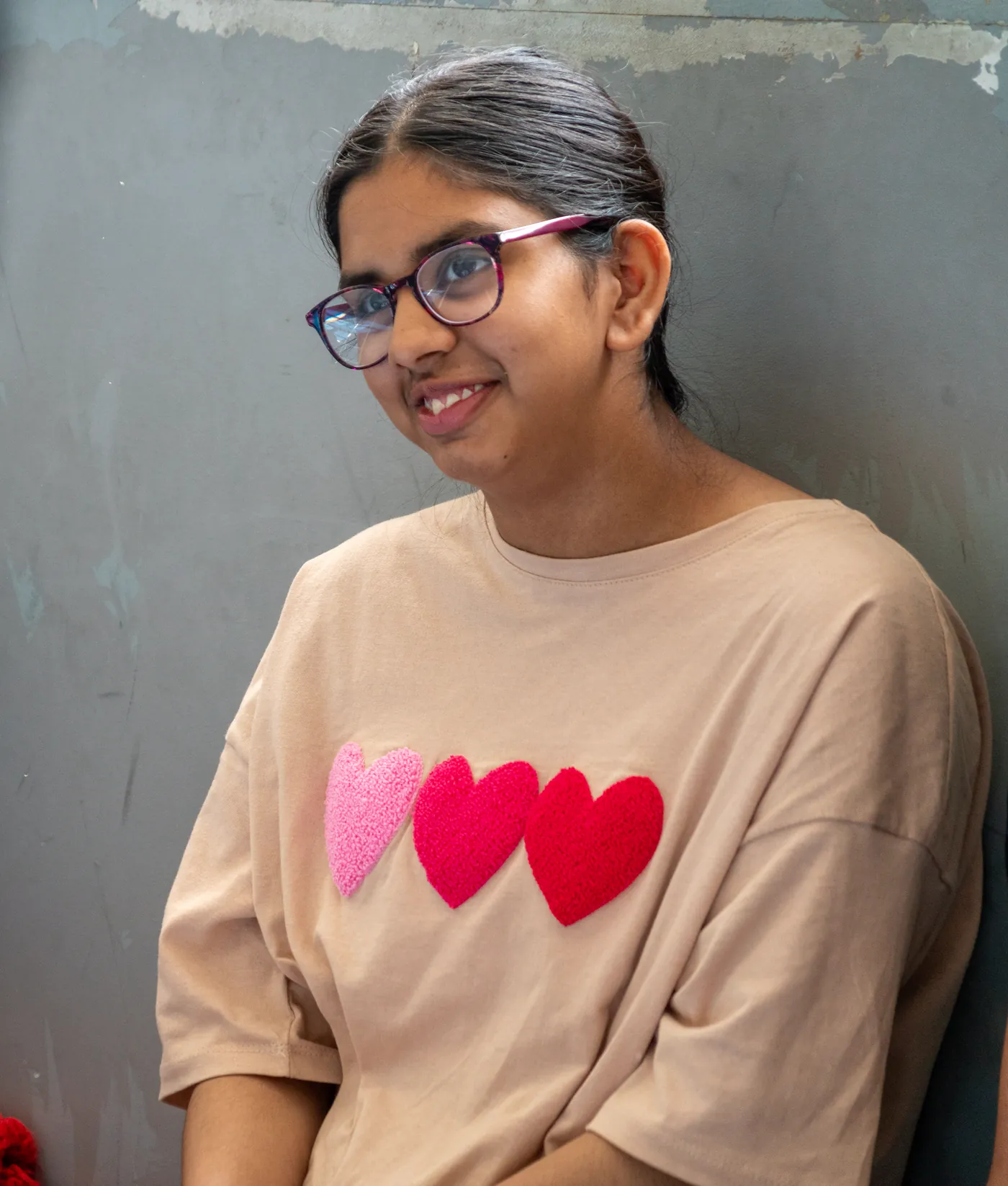 A student in a t-shirt appliquéd with three hearts, leaning against a wall and smiling.